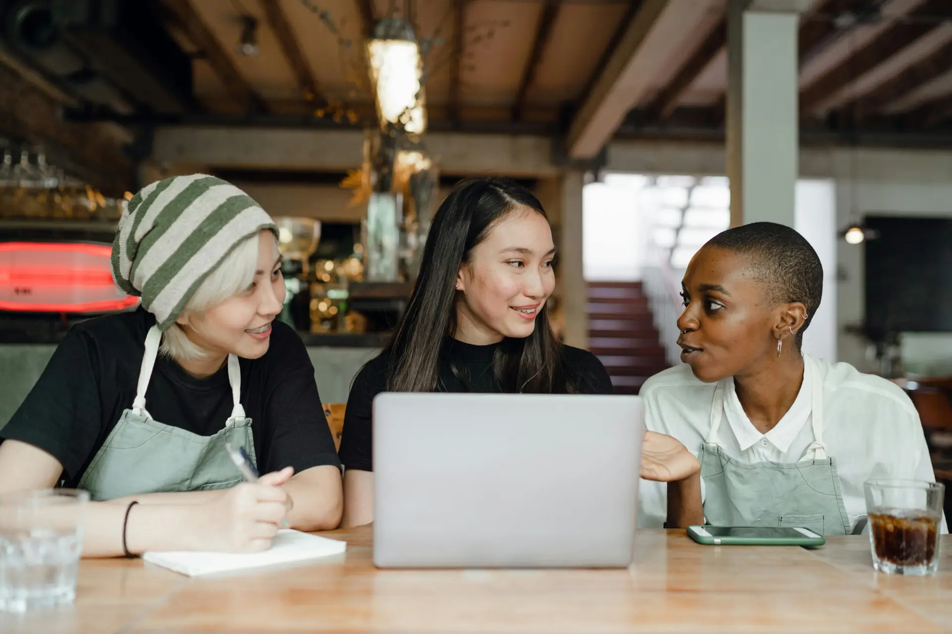 A diverse group of women having a discussion with a laptop in a cozy café environment.